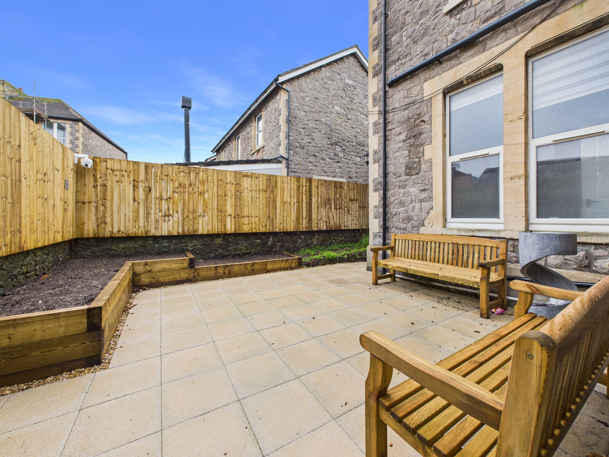 The enclosed rear patio at Beaconsfield House, with wooden benches, raised planting beds and a fenced boundary.