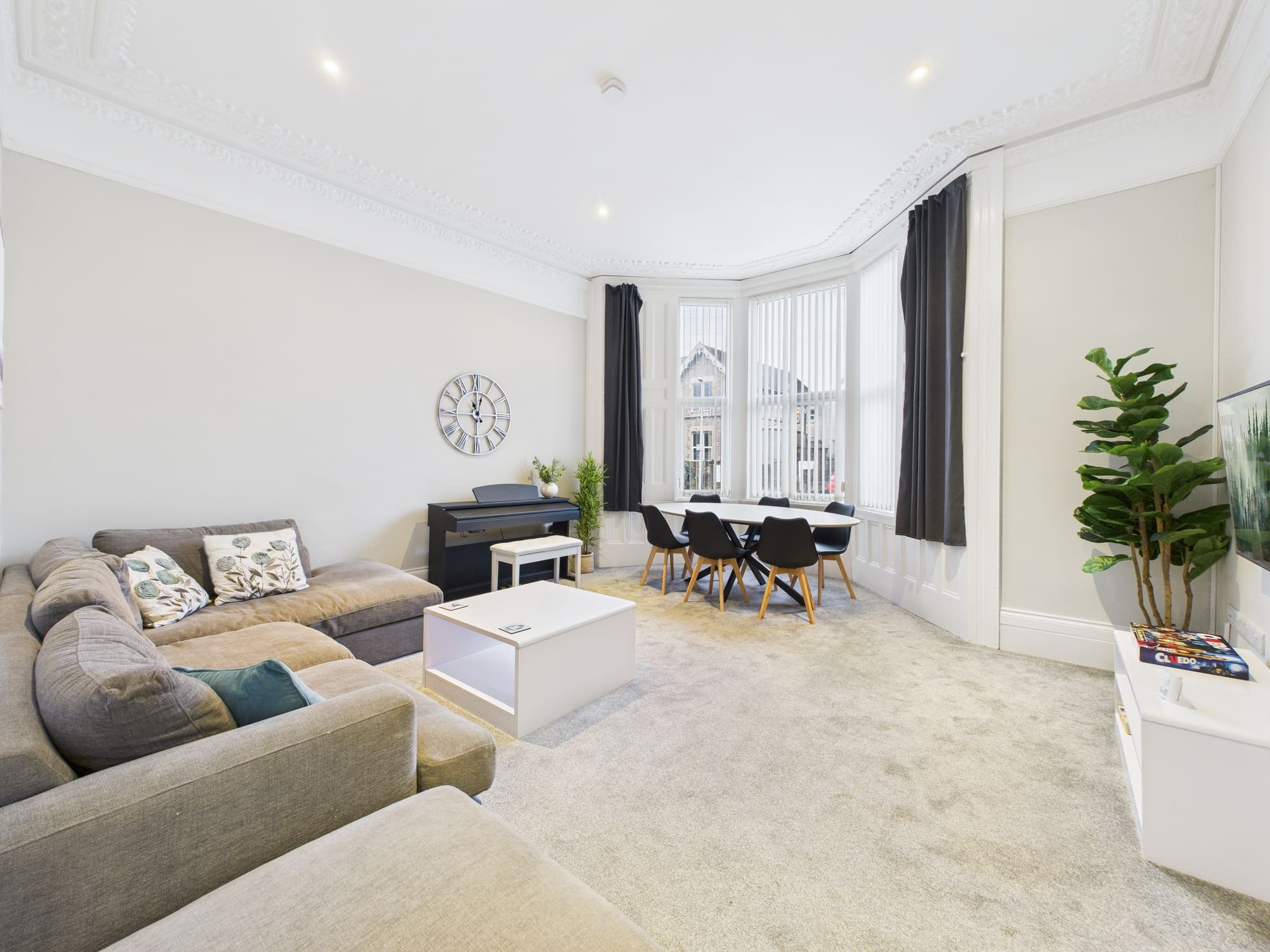 The main lounge at Beaconsfield House, with a large corner sofa, an upright piano and a dining table set in the bay window.